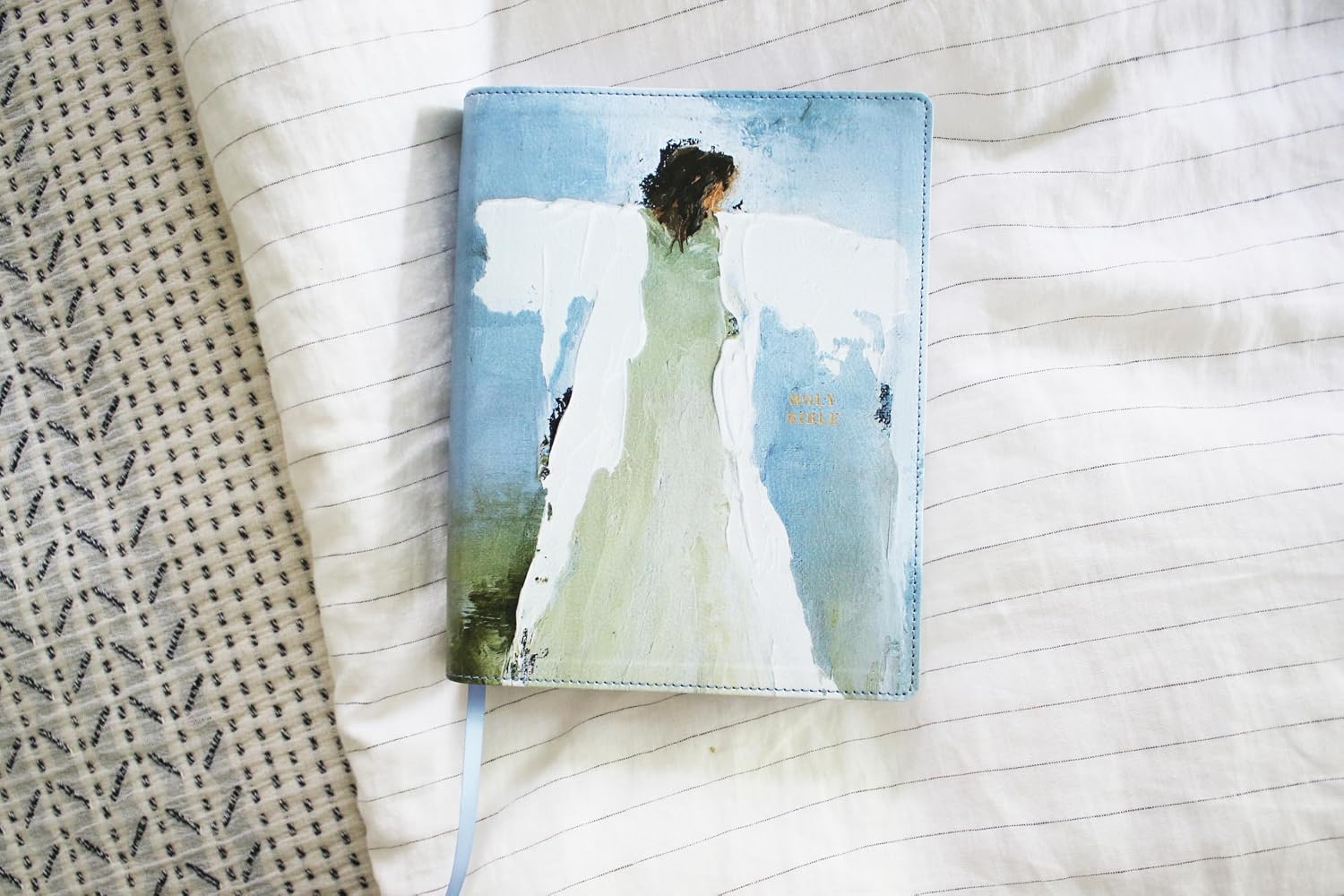 Bible with a cover featuring an artistic illustration of an angel on a textured fabric background.