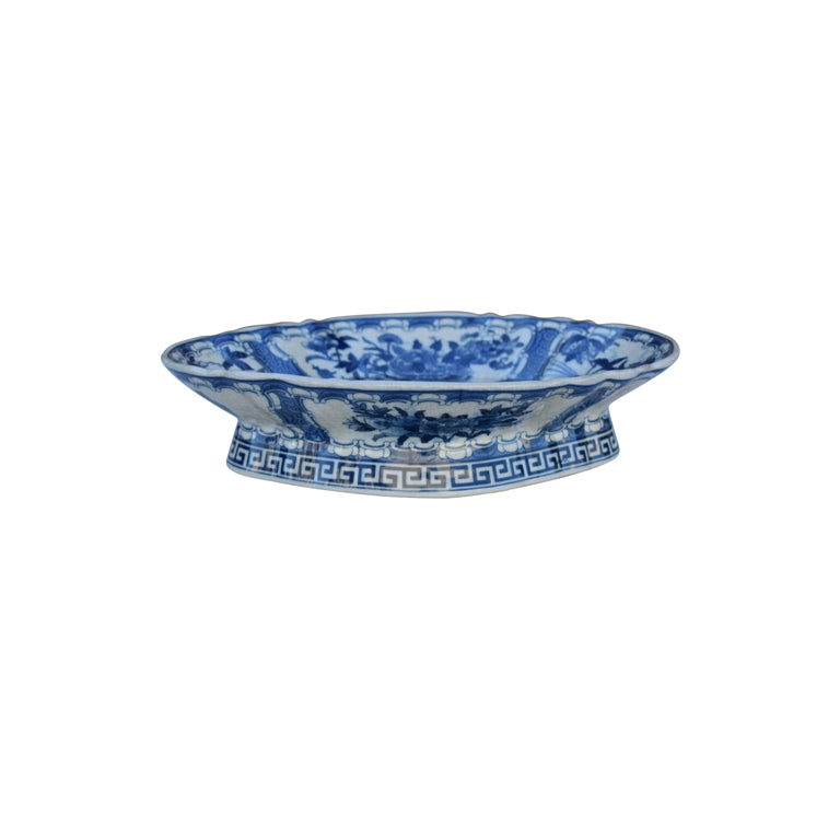 A blue and white porcelain pedestal plate with traditional Chinese landscape and floral patterns, set against a plain white background.