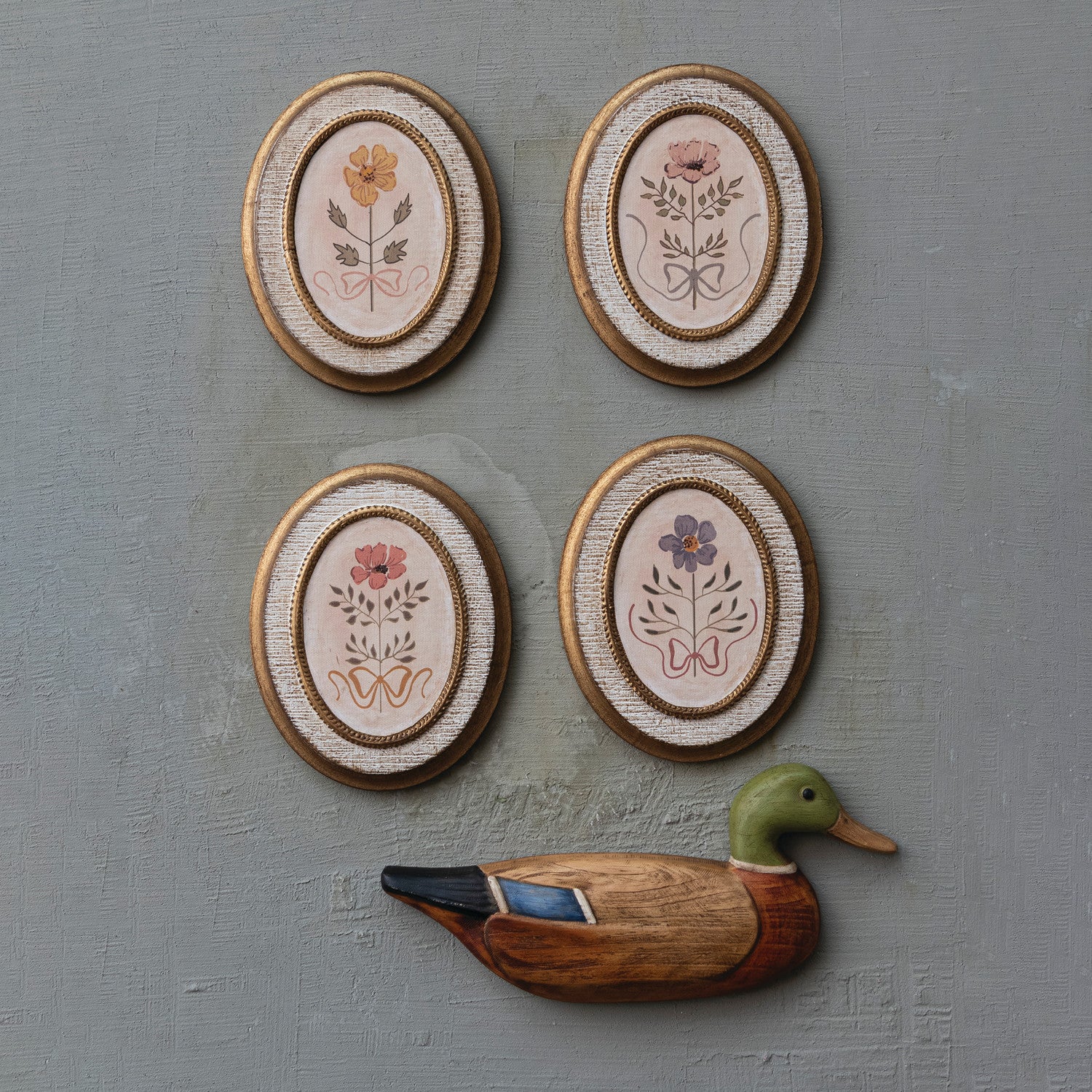 Four oval wall decorations with floral patterns and a wooden duck figurine on a gray background