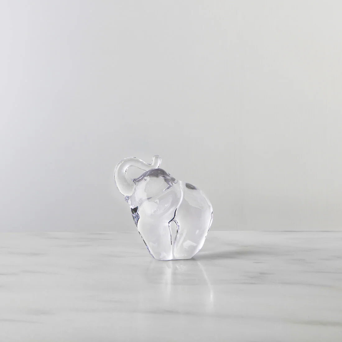Clear glass elephant figurine on a light gray surface with a light gray background