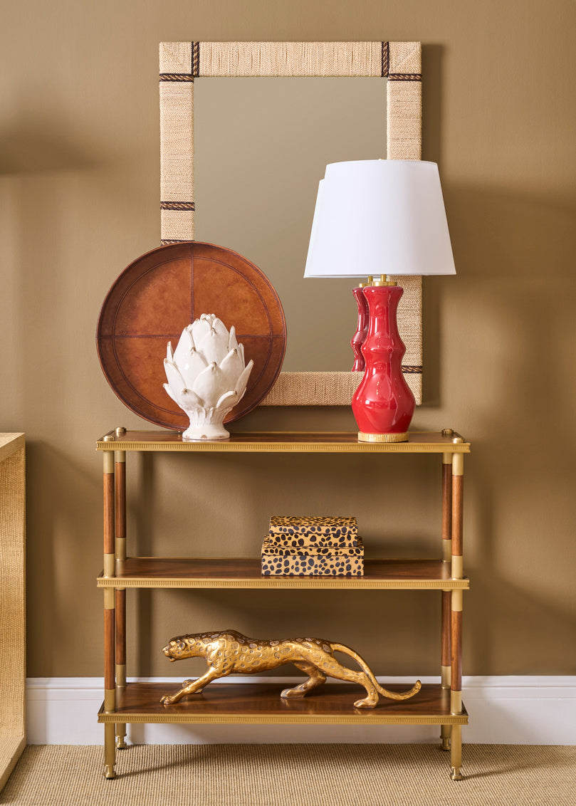 Decorative shelf with a lamp, mirror, and sculptures against a beige wall.