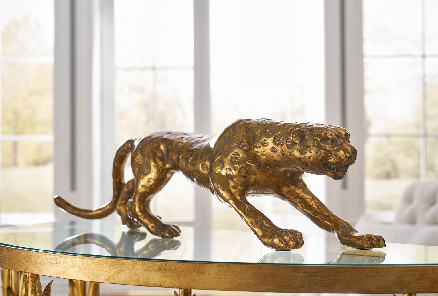 Gold leopard figurine on a glass table with a blurred window background