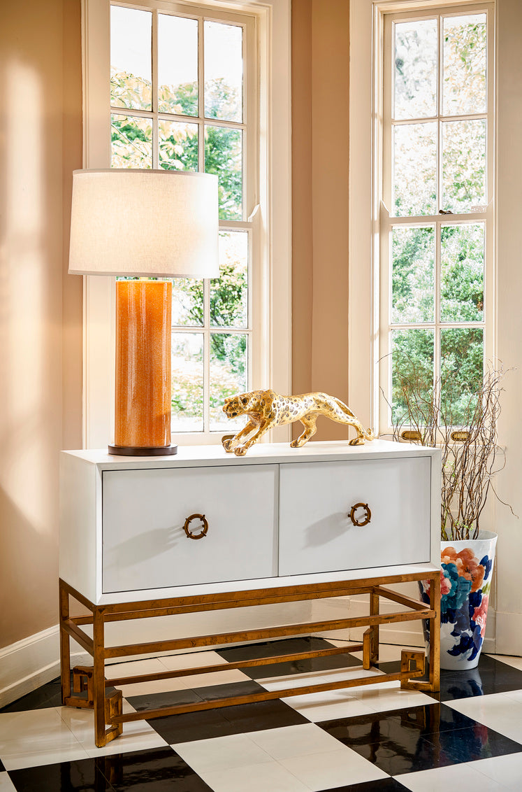 White console table with gold accents in a room with large windows and decorative items.