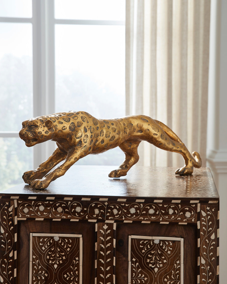 Gold leopard figurine on a decorative wooden cabinet with white curtains in the background