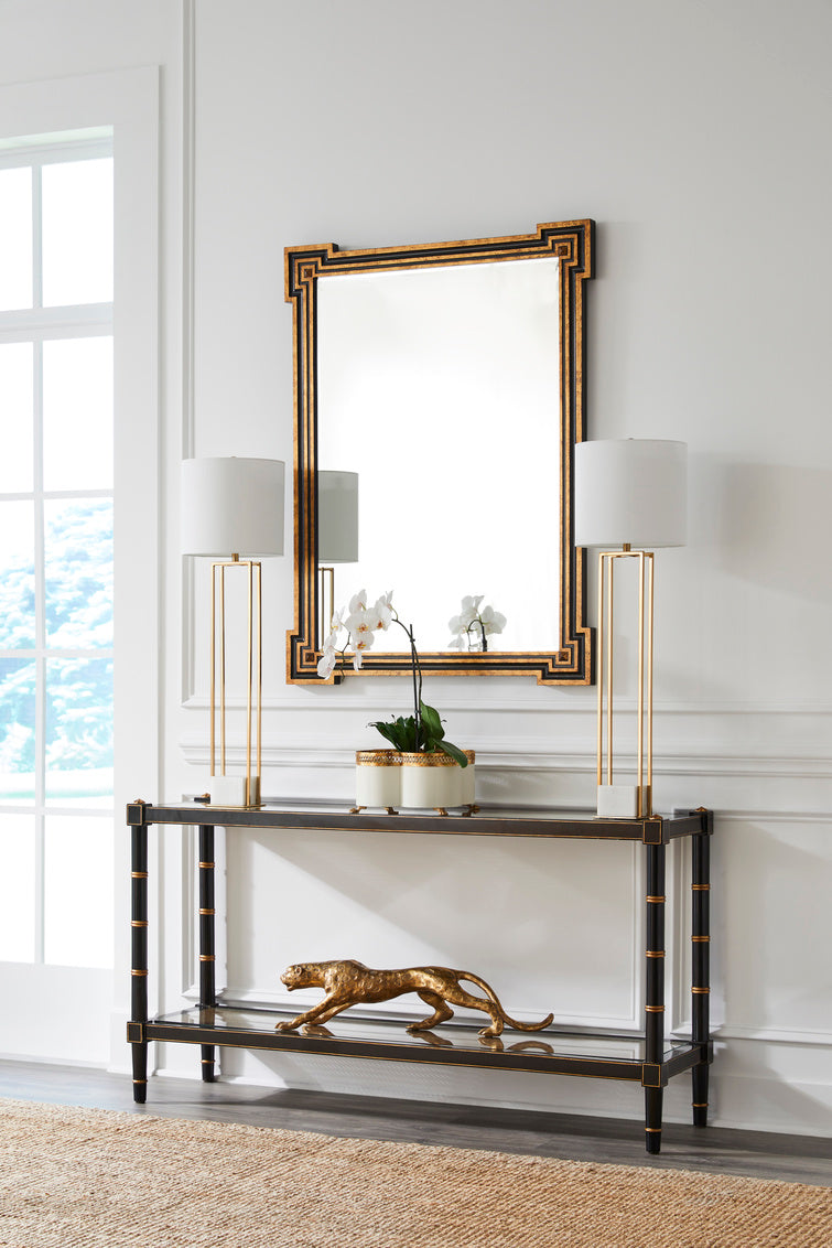 Console table with decorative items in a room with a large mirror and lamps.