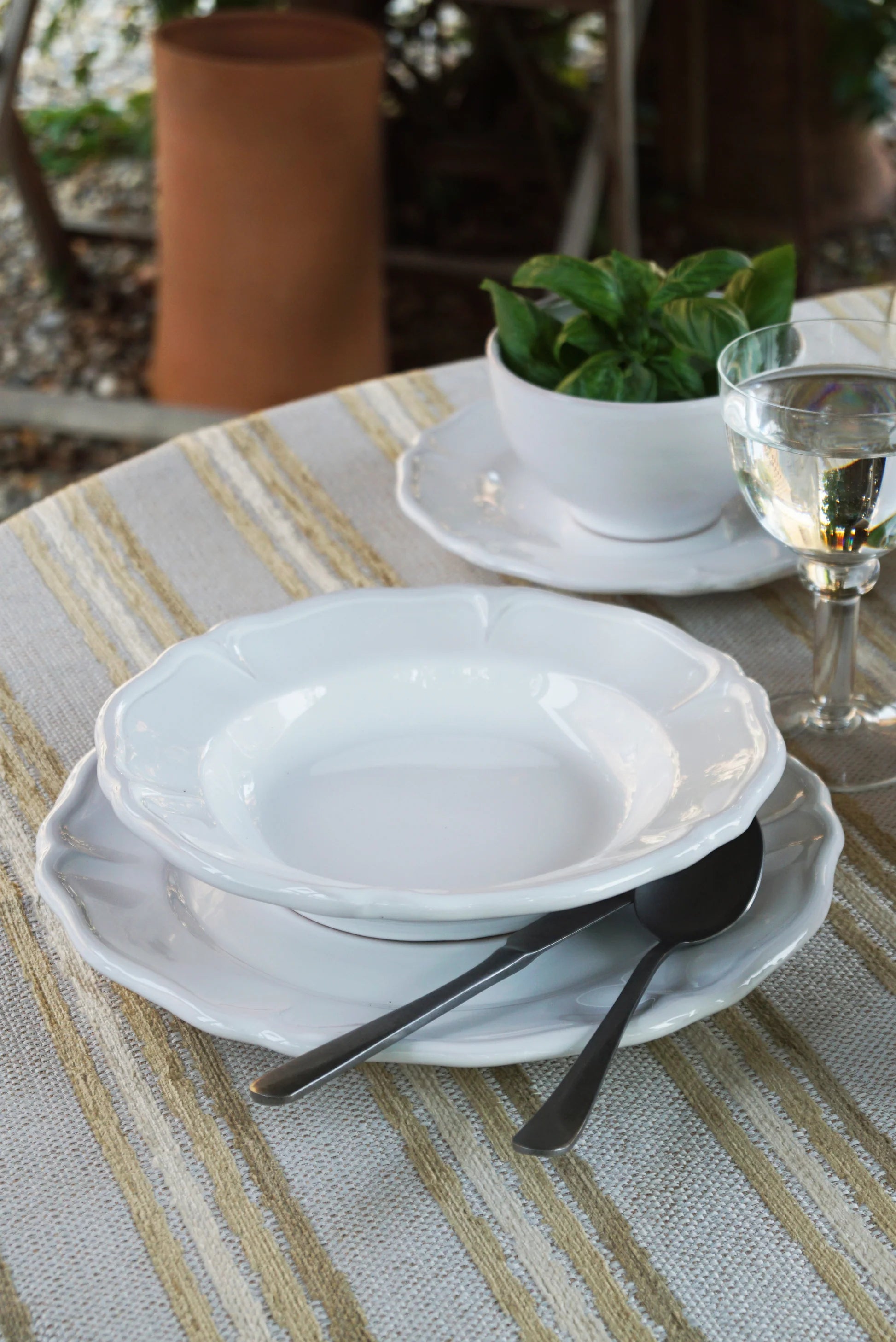 White ceramic dishes with black cutlery on a striped tablecloth outdoors.