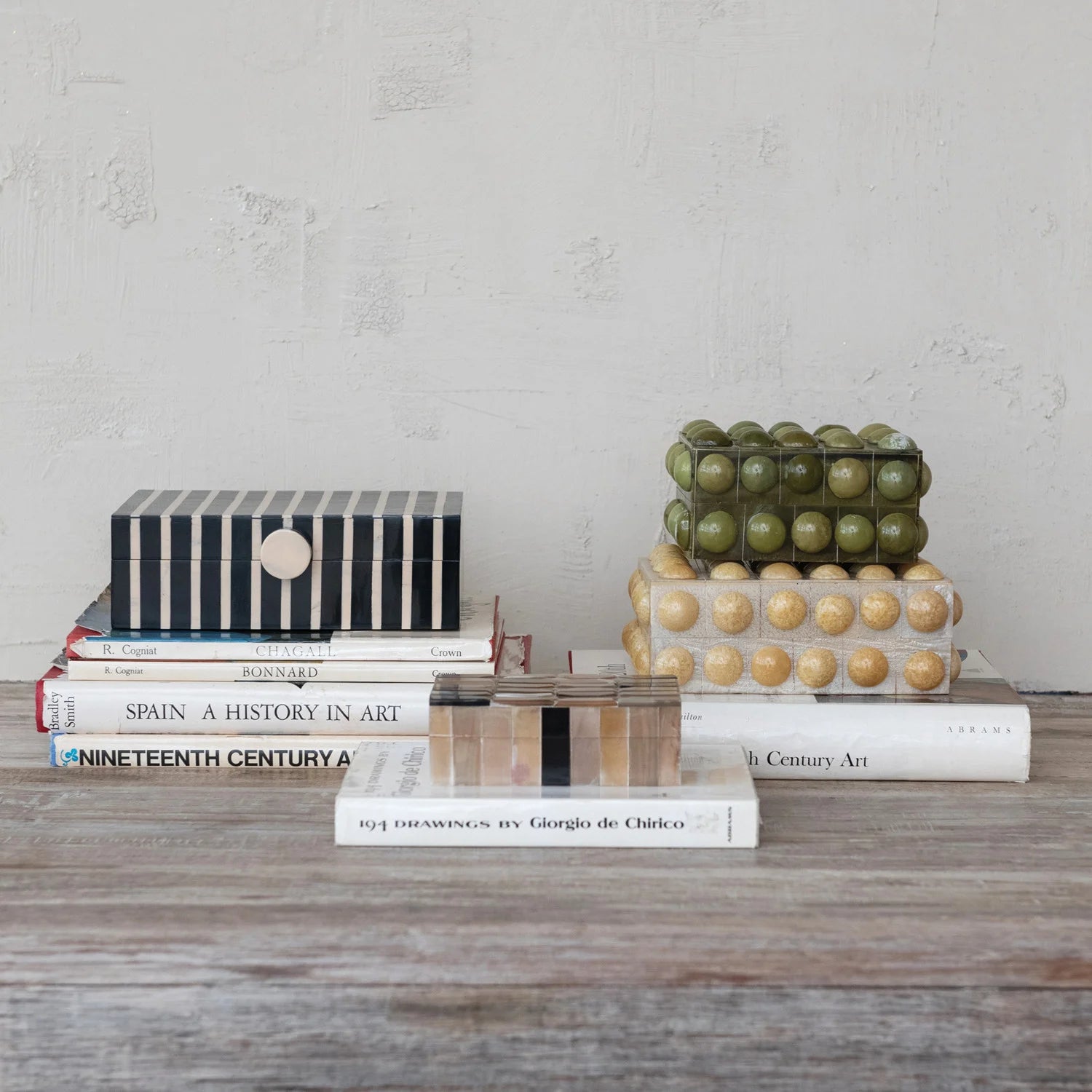 Stack of books on a wooden surface with decorative objects against a gray wall.
