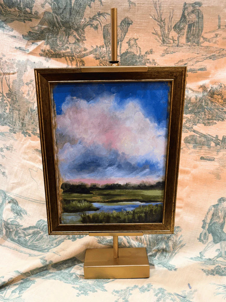 Small landscape painting on a gold easel against a decorative wallpaper background