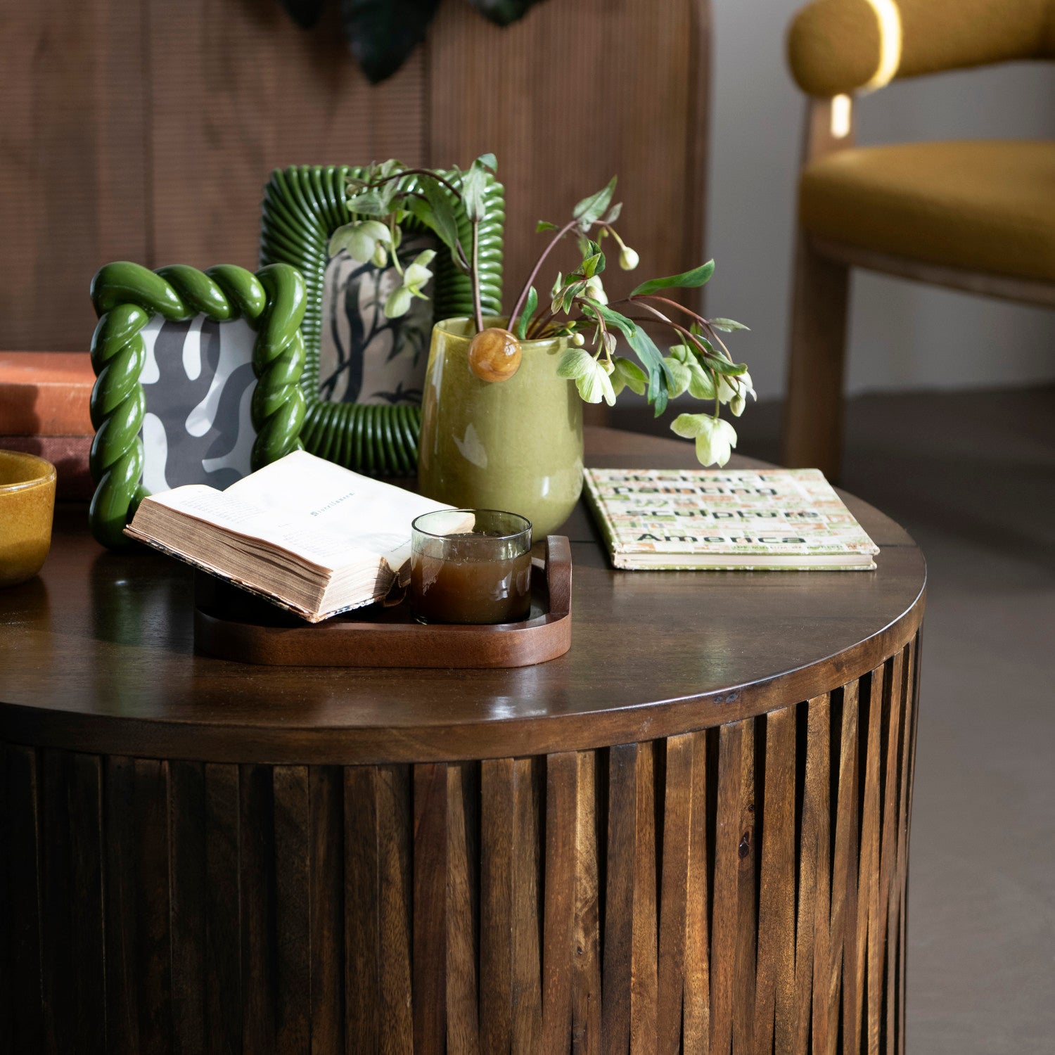 Wooden table with decorative items including a book, candle, and vases in a cozy room.