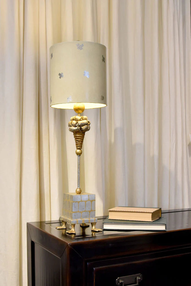 Decorative table lamp with a beige shade on a wooden surface with curtains in the background