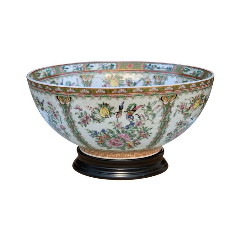 A large decorative porcelain bowl with a hand-painted floral and bird pattern on a white background, resting on a dark wooden pedestal against a plain white backdrop.