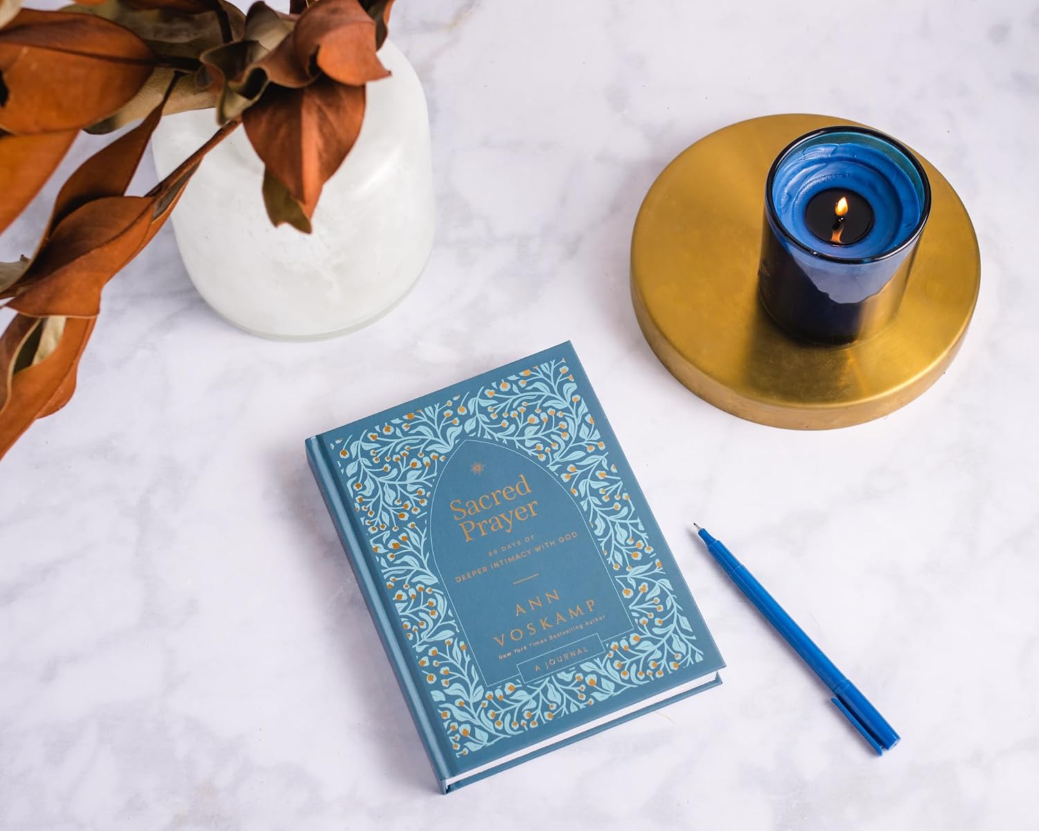 Blue book on marble top with pen and candle beside it.