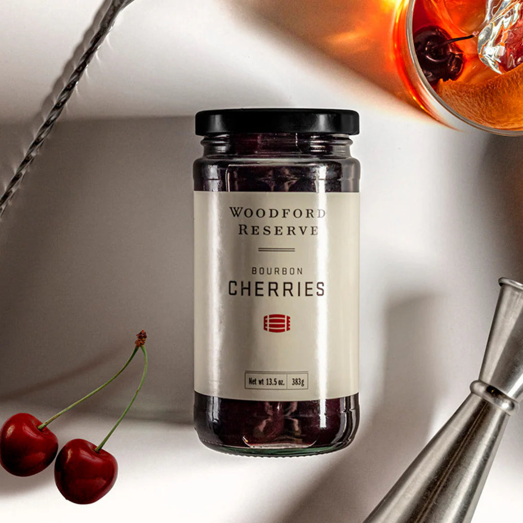 Jar of Woodford Reserve bourbon cherries with cherries and a glass on a white background
