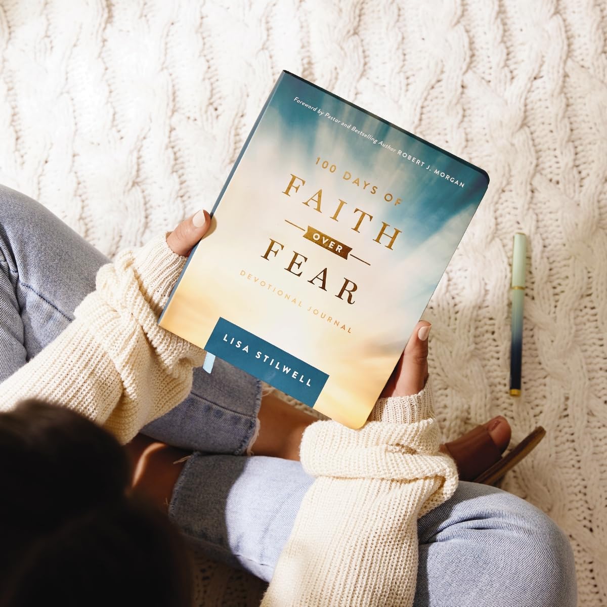 Person holding a book titled '100 Days of Faith Over Fear' by Lisa Stilwell against a textured white background.