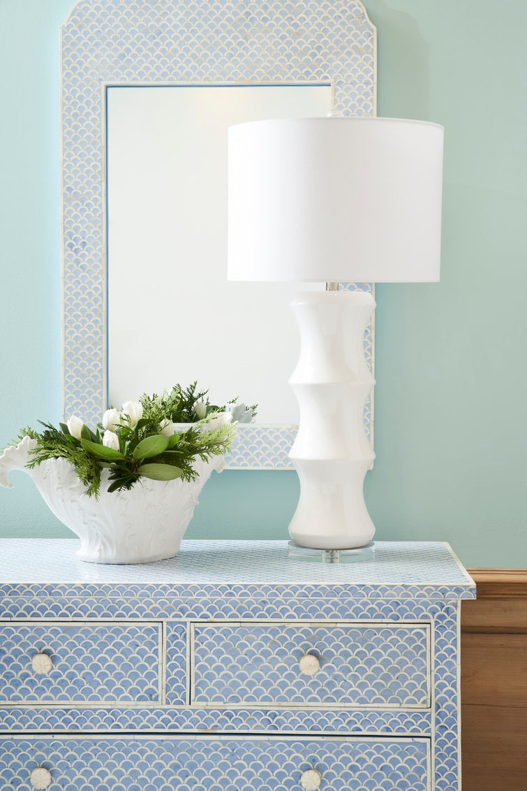 Decorative dresser with a white lamp, decorative bowl, and mirror in a room with light blue walls.
