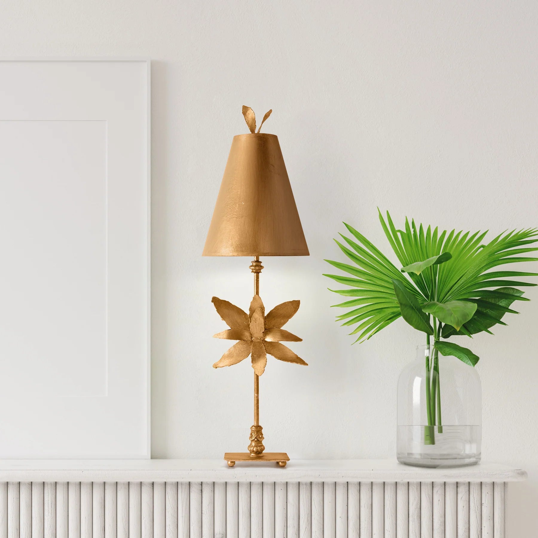 Gold decorative lamp with leaf design next to a vase with green leaves on a white surface.