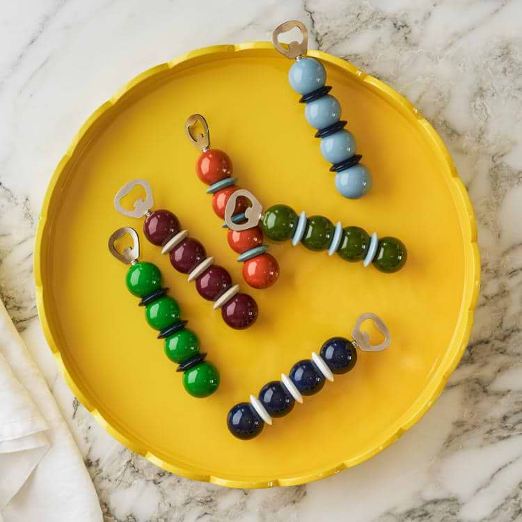Colorful beaded bottle openers on a yellow plate with a marble background