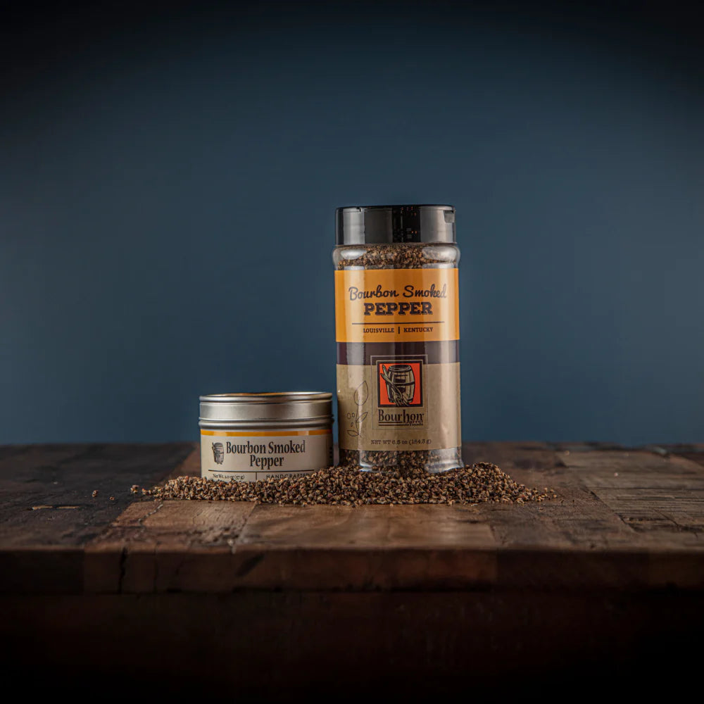 Two containers of bourbon smoked pepper on a wooden surface with a dark background