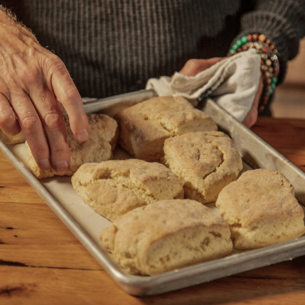 Baked goods on a tray with a person holding it, wearing a textured sweater and colorful bracelets.
