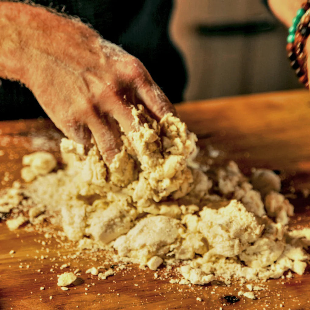 Hand kneading dough on a wooden surface with a blurred background