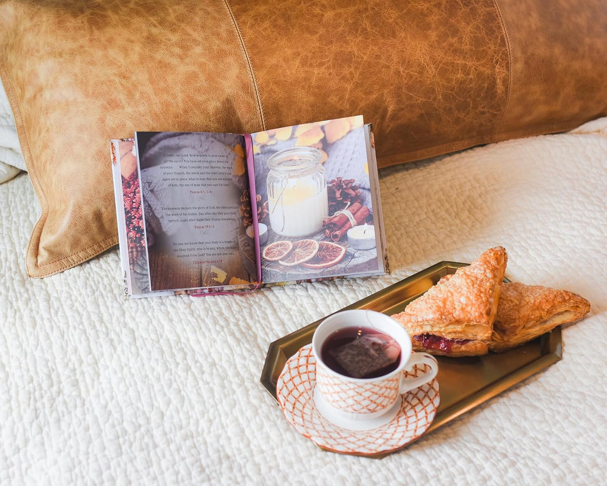 Tray with a cup of tea, pastries, and an open book on a bed.