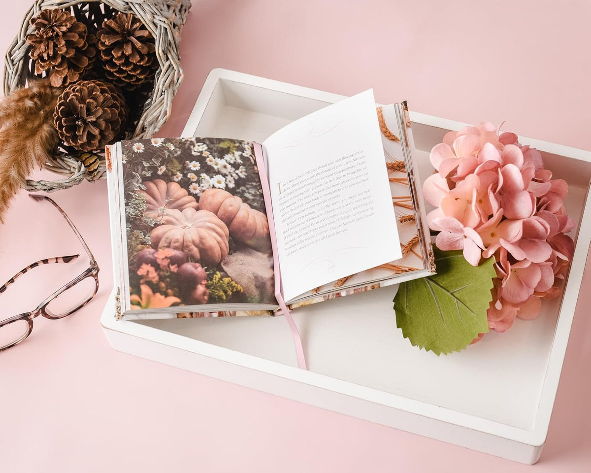 Open book with floral design on a pink surface with flowers and glasses.