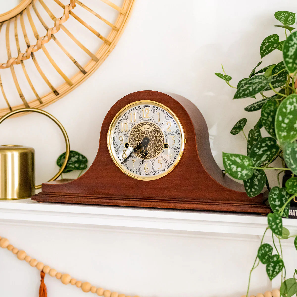 Wooden mantel clock on a white shelf with decorative elements and plants.