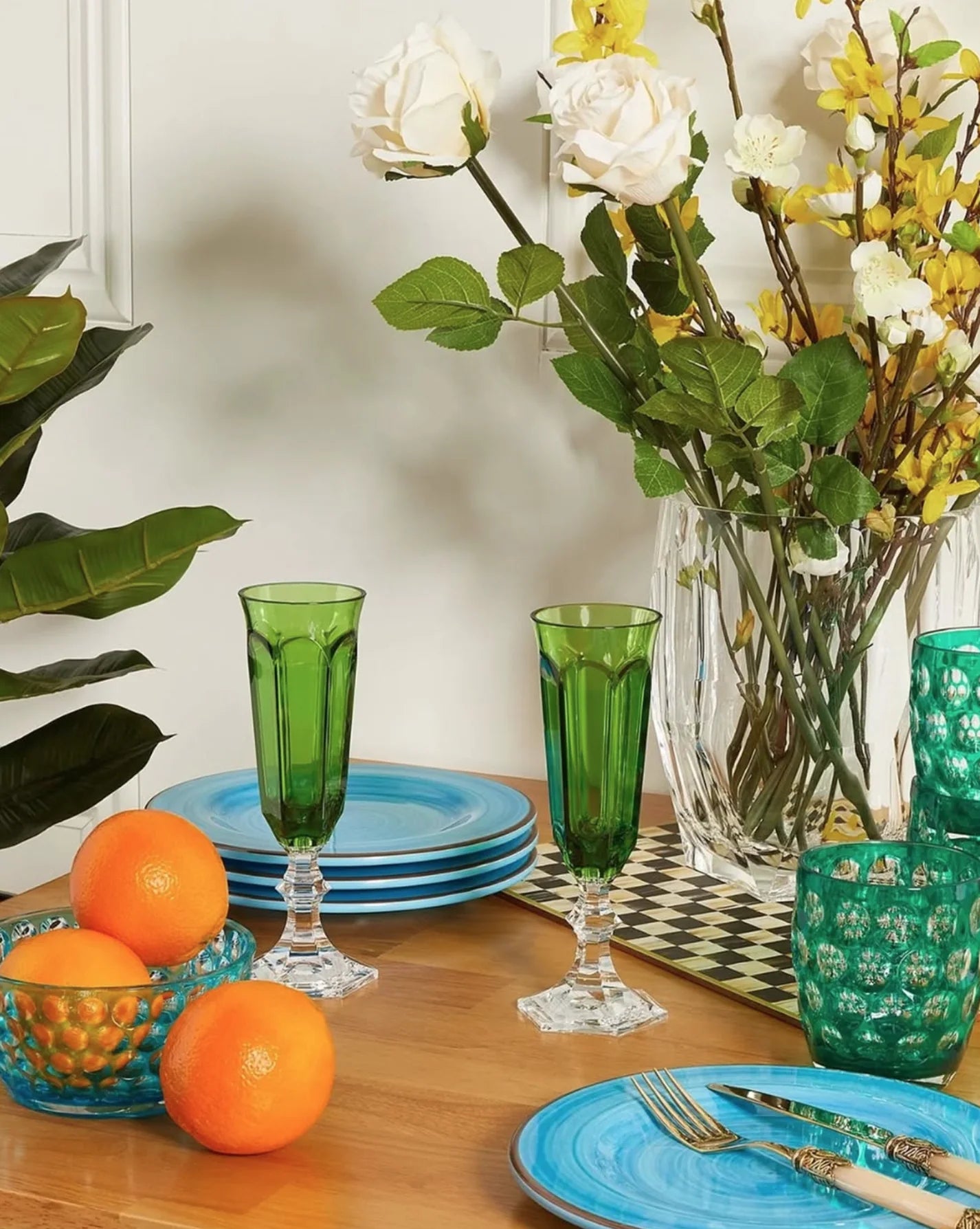 Dining table setting with green glasses, blue plates, and a vase of flowers.
