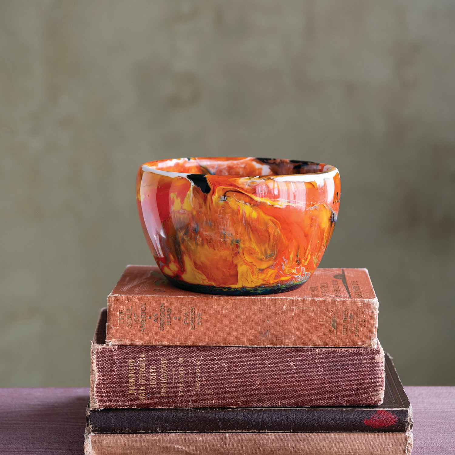 Decorative bowl with orange and yellow patterns on a stack of books against a neutral background