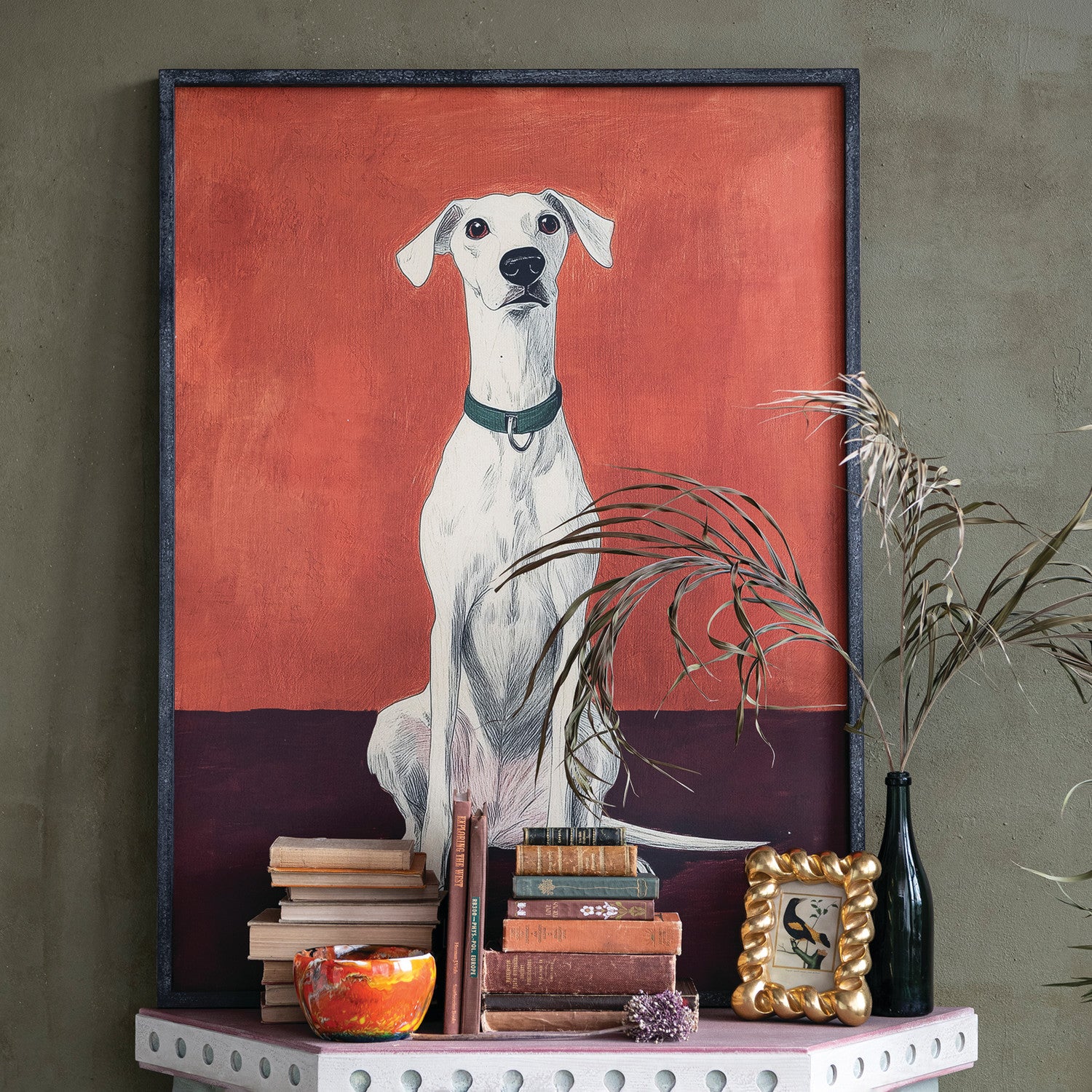 Framed artwork of a dog on a shelf with books and decorative items.