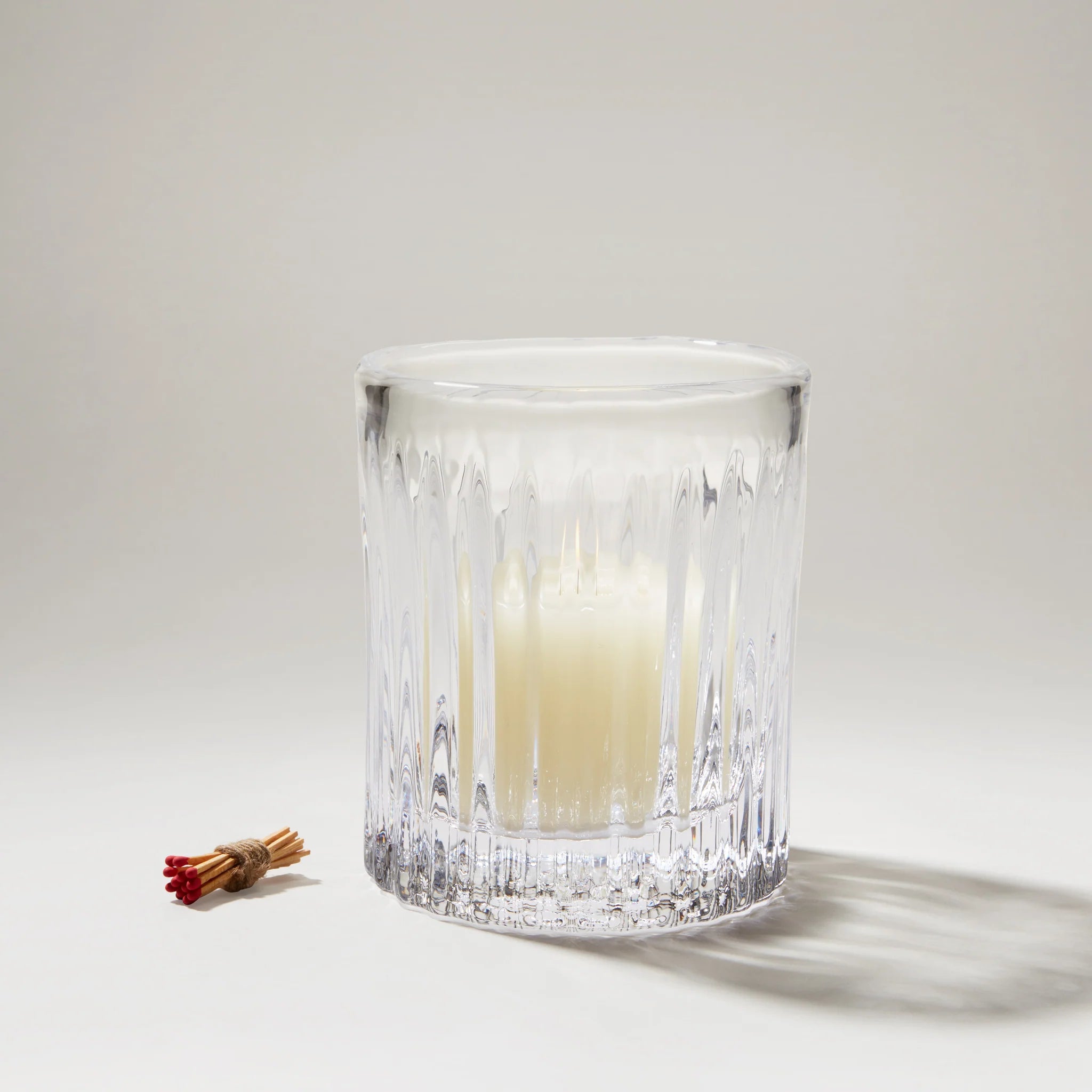 Clear glass candle holder with a lit candle on a white background