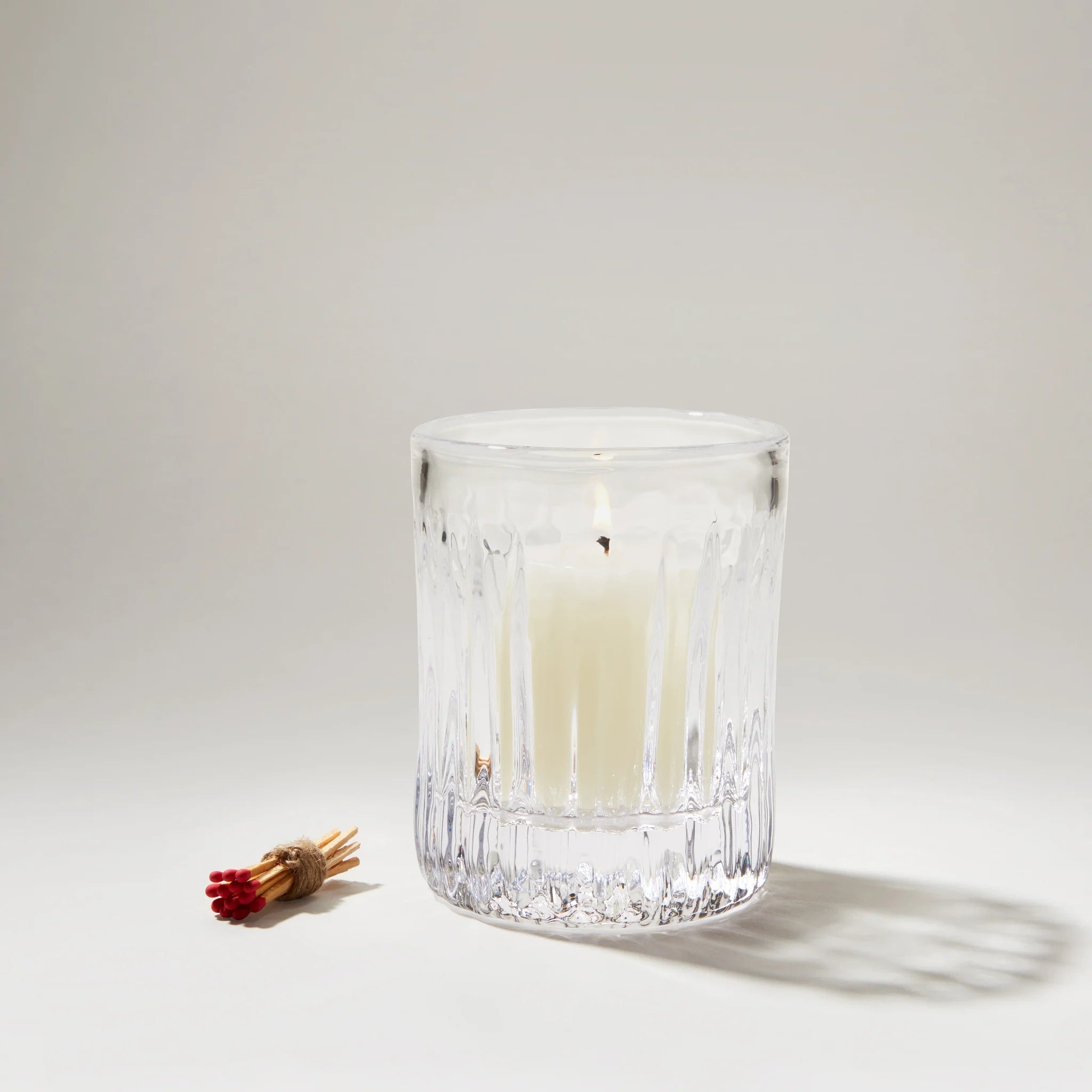 Clear glass candle holder with a white candle on a light gray background