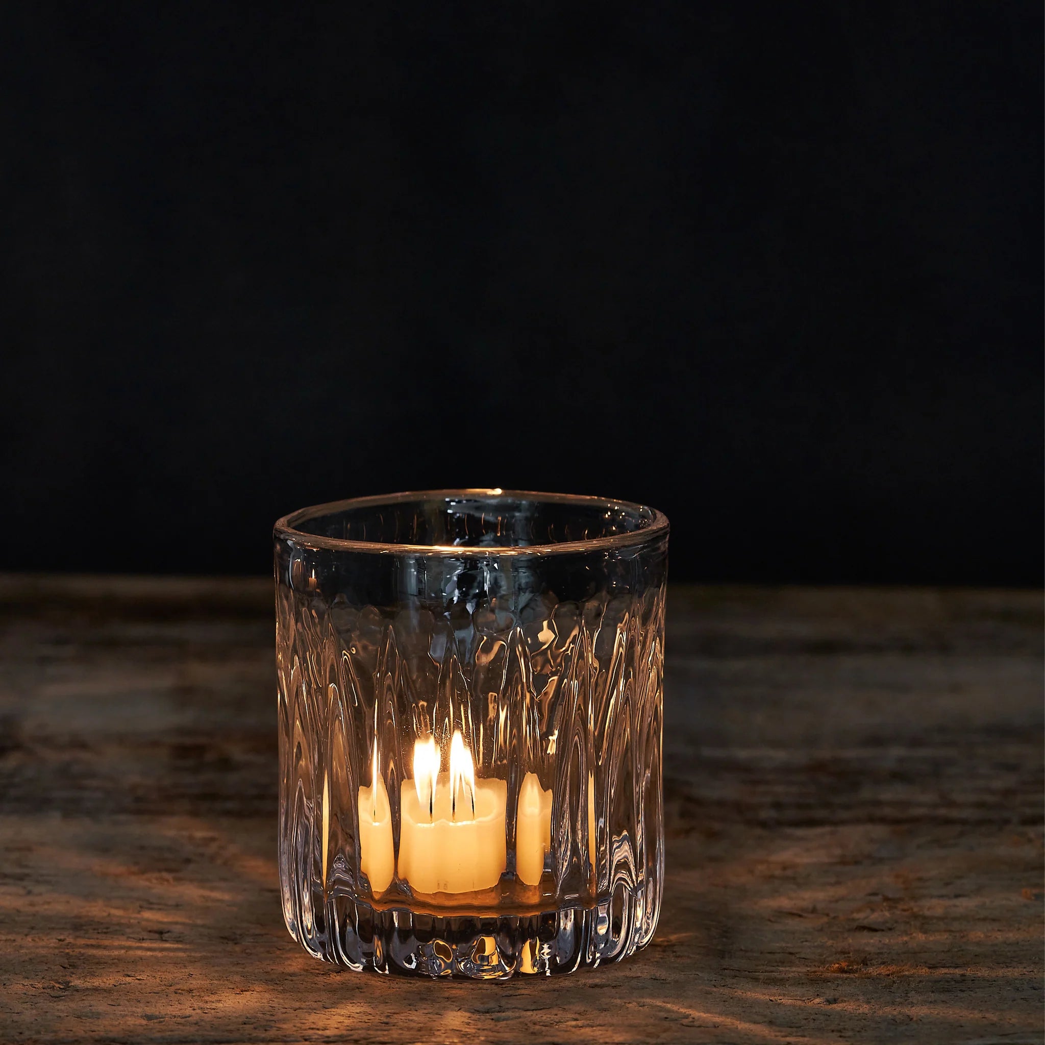Glass candle holder with a lit candle on a dark background