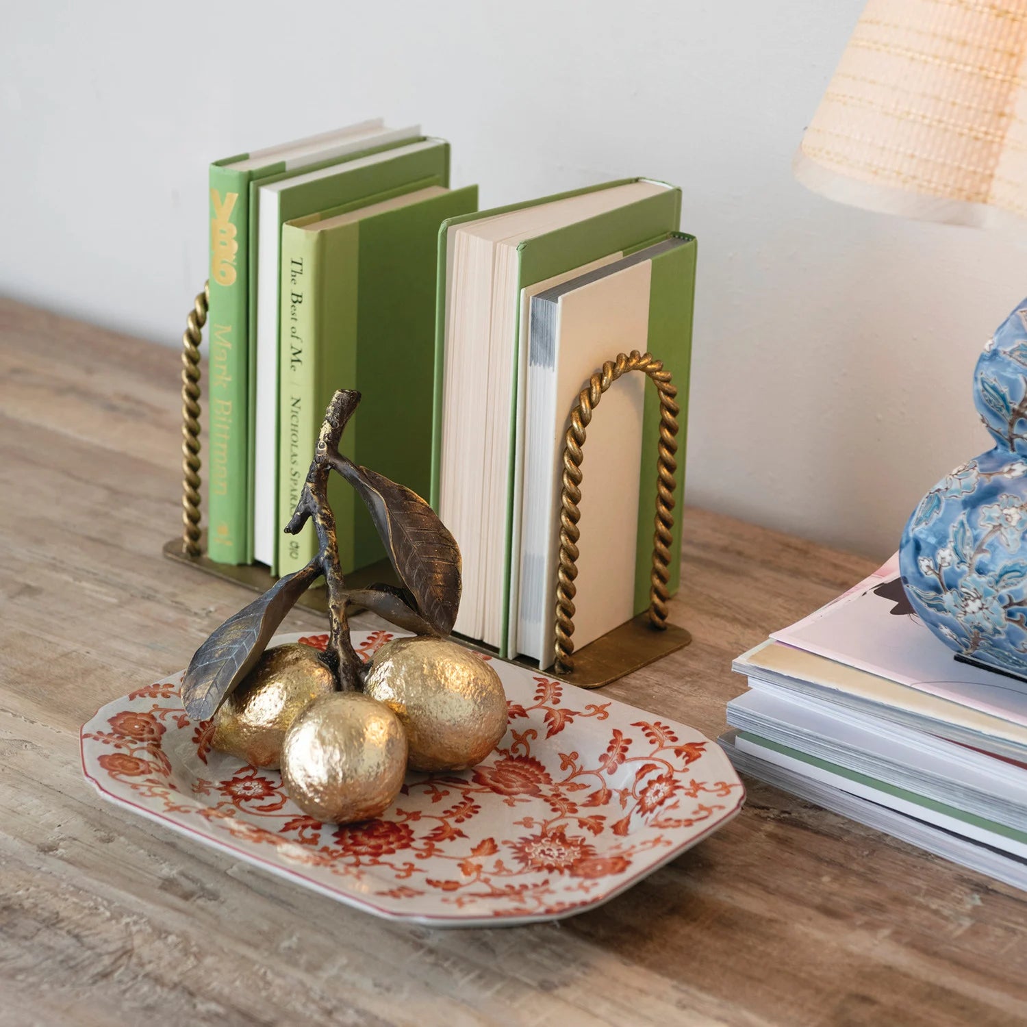 Decorative setup with books, gold fruit figurines, and a plate on a wooden surface.