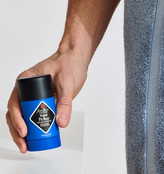 Hand holding a blue deodorant stick next to a gray towel on a white background