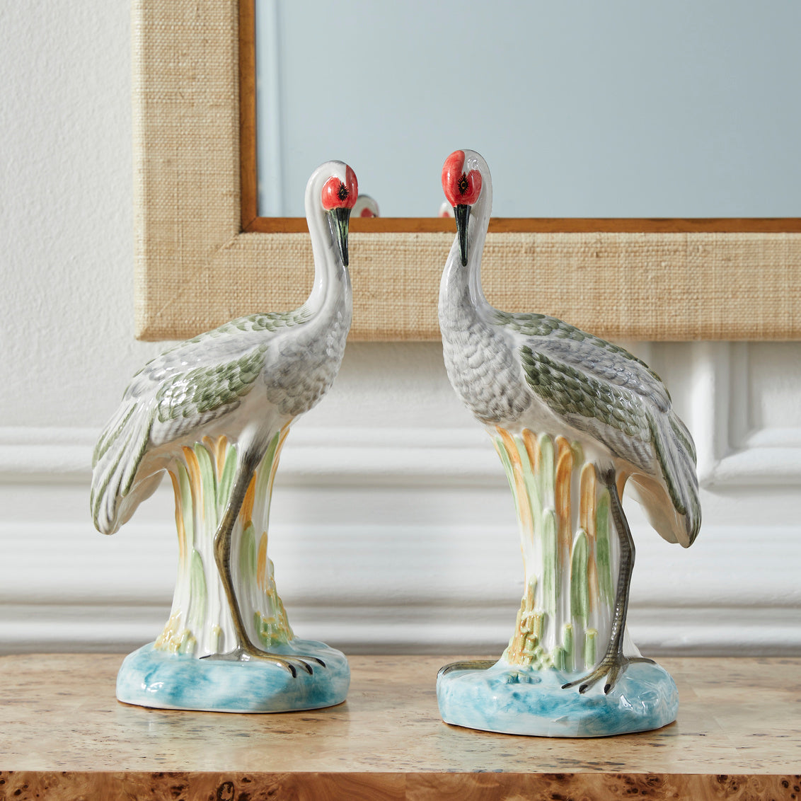Two ceramic crane figurines on a wooden surface with a neutral background
