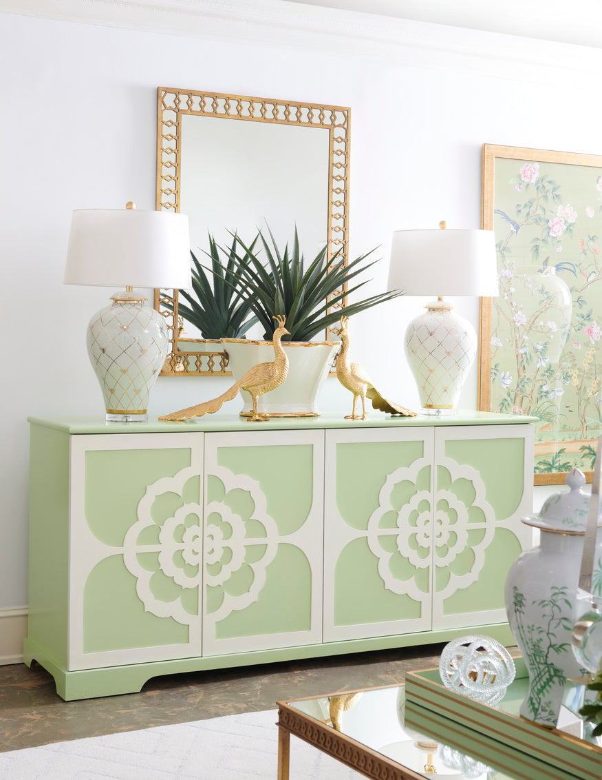 Decorative green sideboard with white floral patterns, lamps, and a peacock figurine in a room.