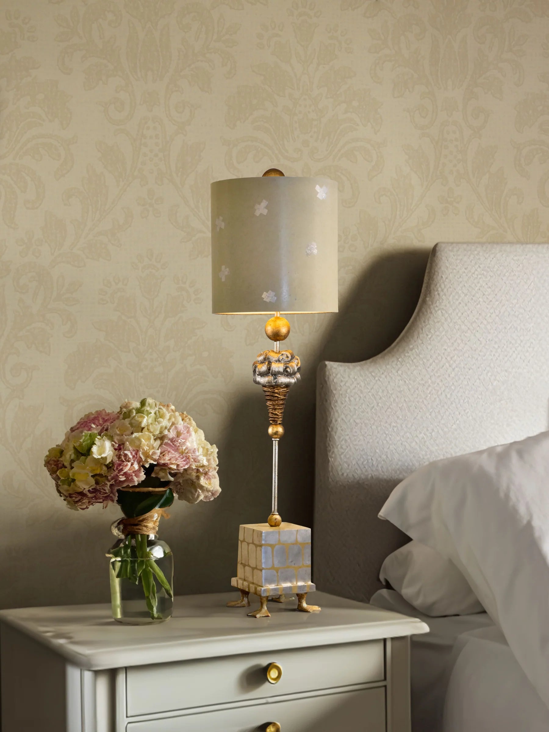Decorative lamp on a nightstand next to a bed with floral arrangement