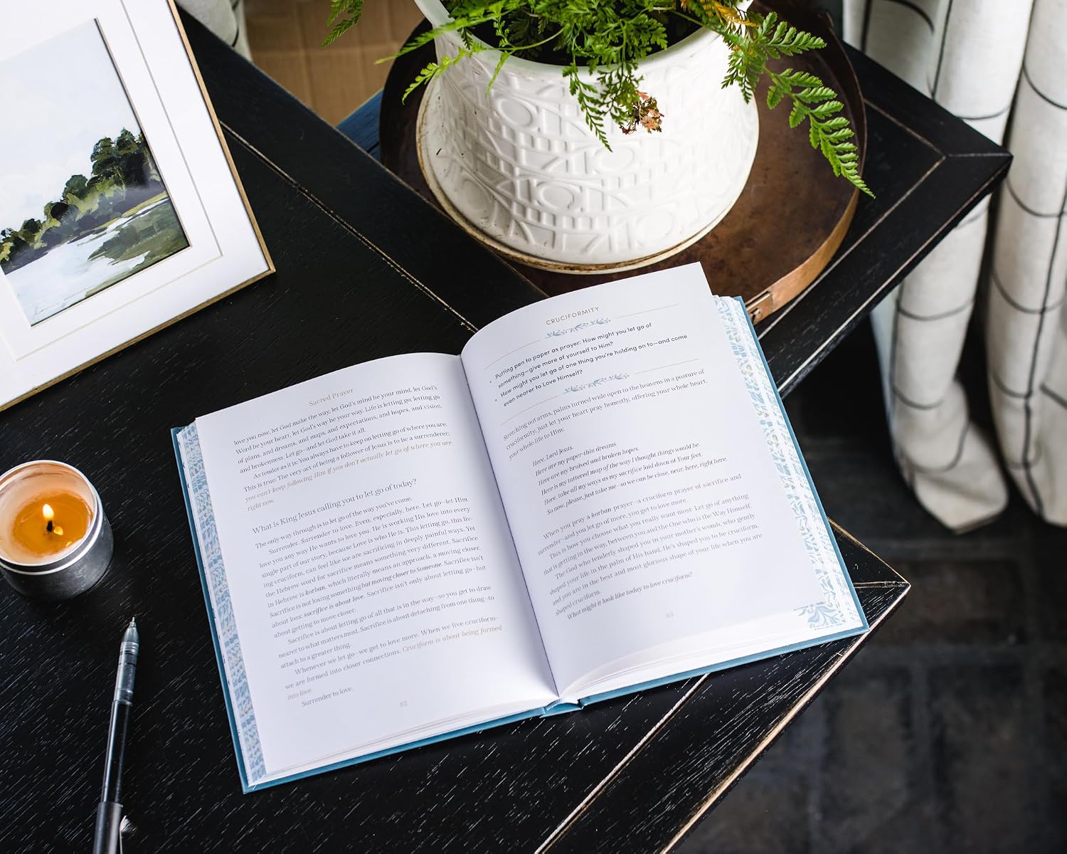 Open book on a dark surface with a candle and framed picture in the background