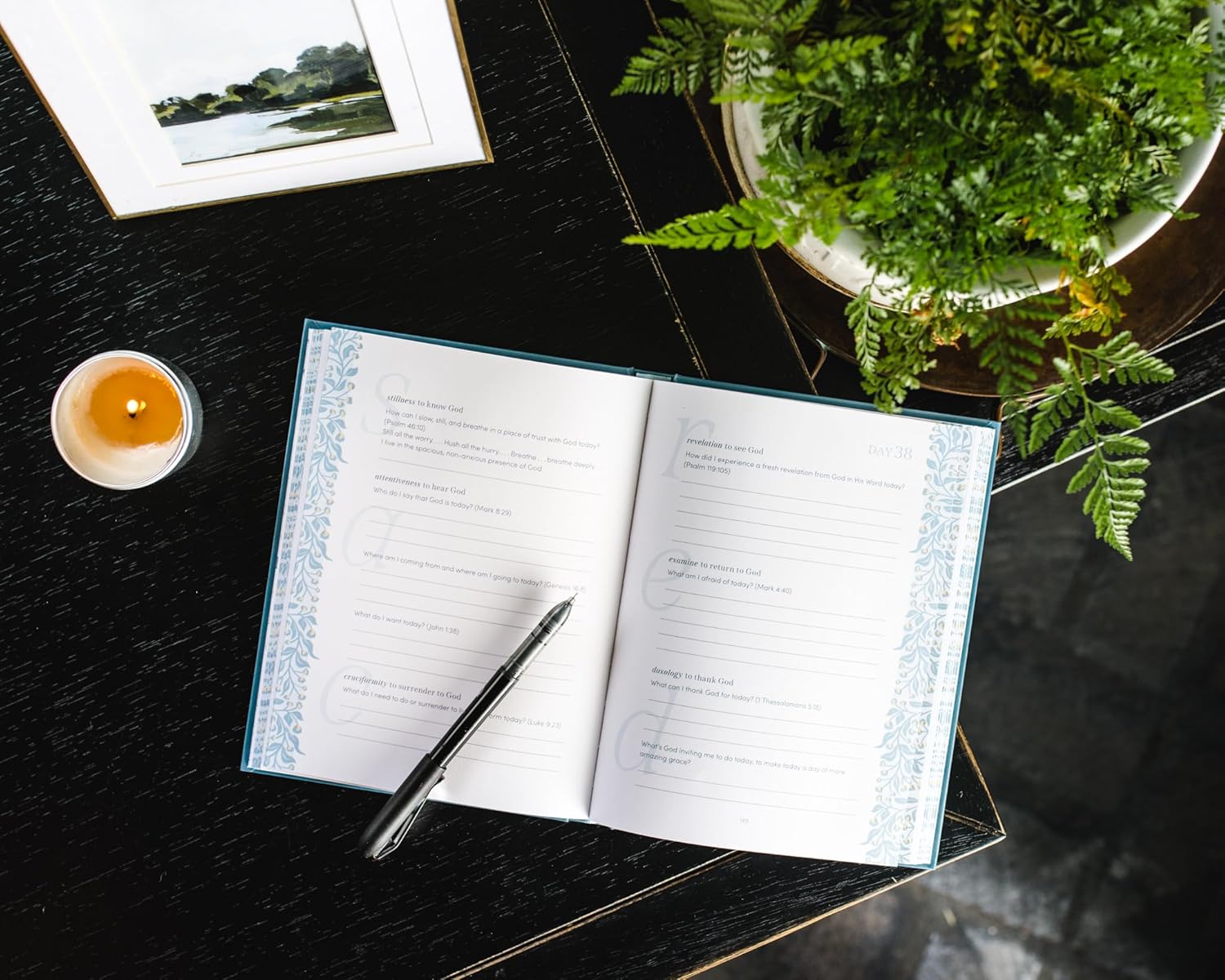 Open notebook with pen on a dark surface with a plant and candle