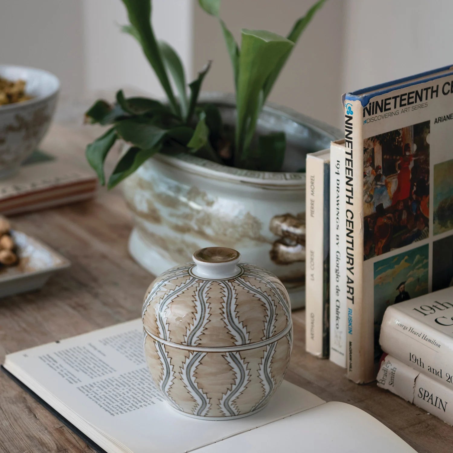 Decorative vase on an open book with a plant and books in the background