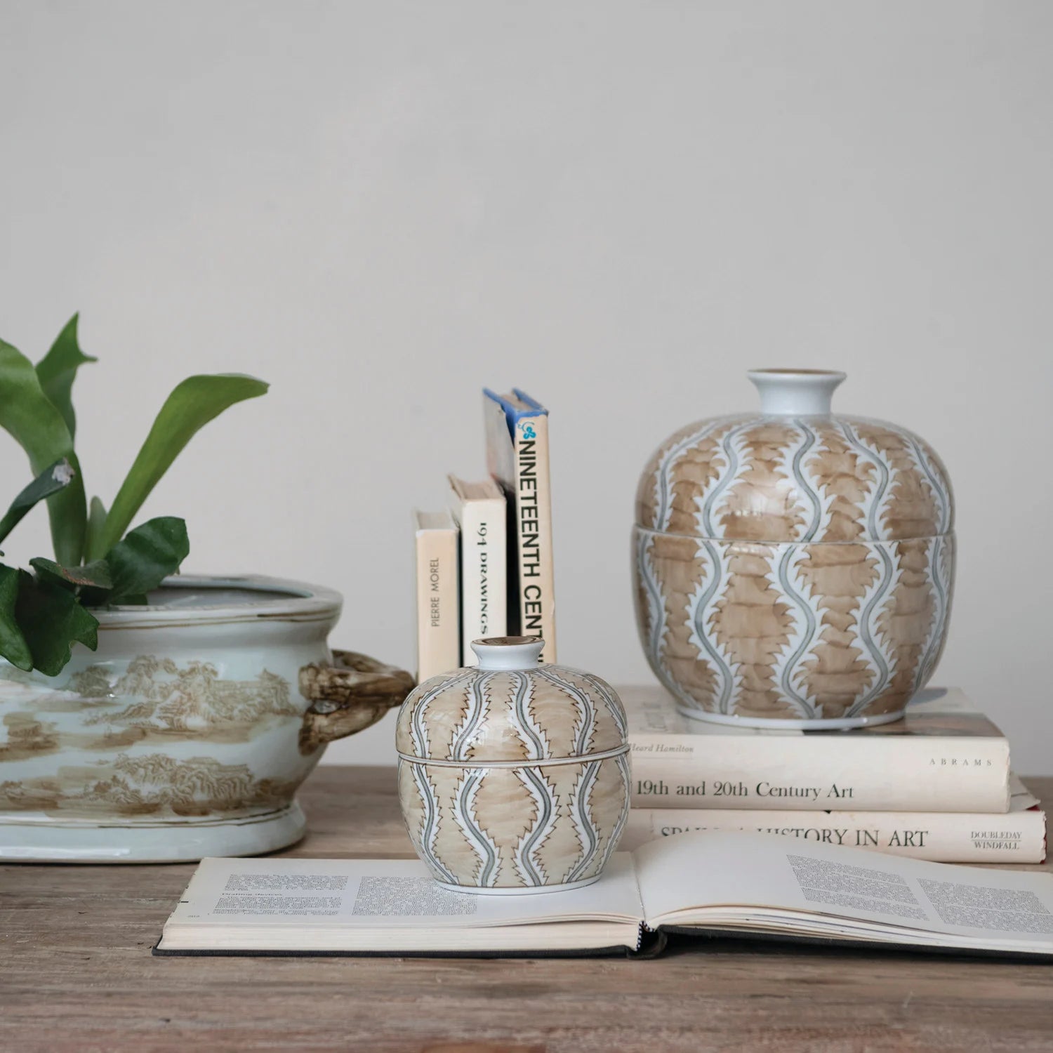 Decorative vases with wavy patterns on a wooden surface with books and a plant.