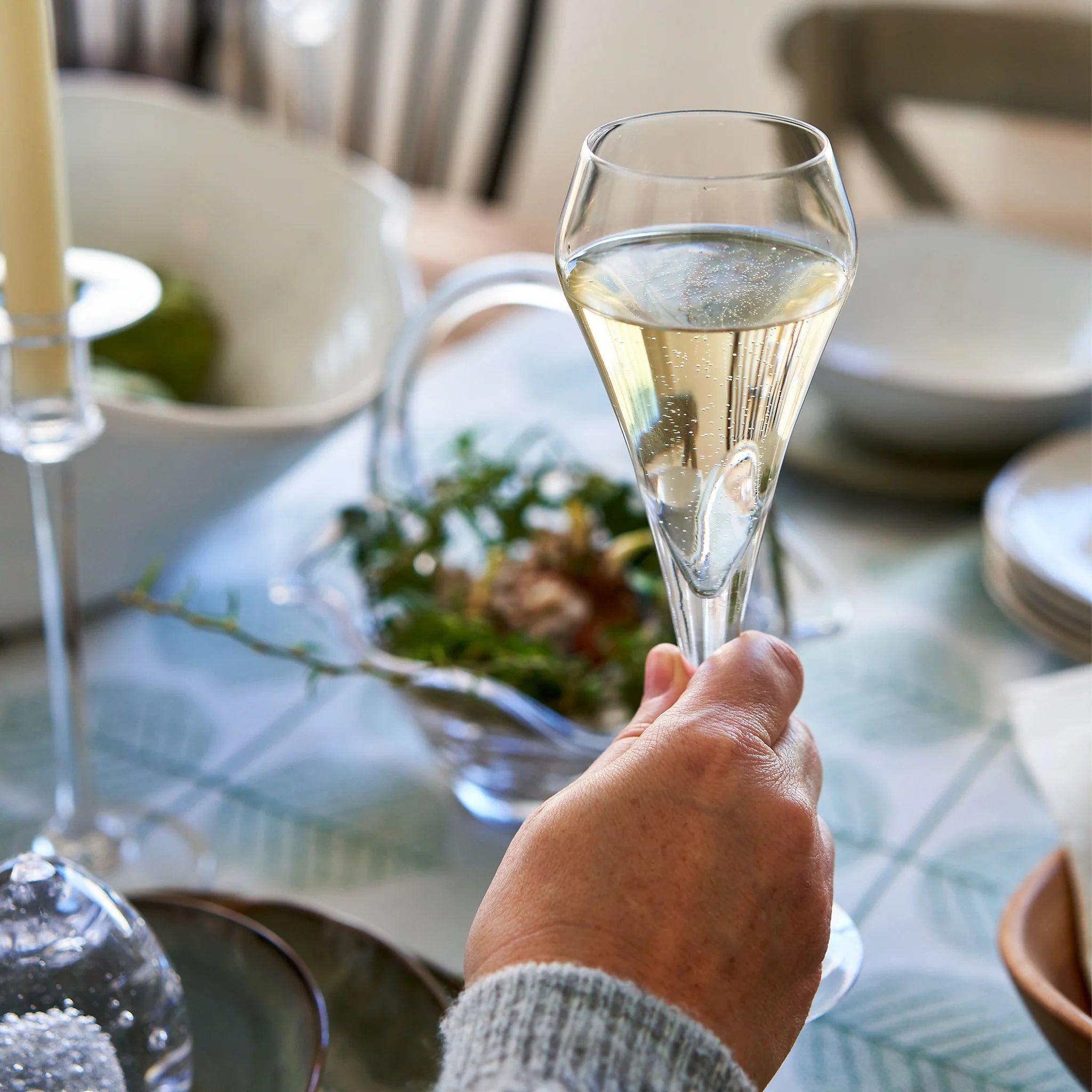 Hand holding a glass of champagne on a dining table with a festive setting.