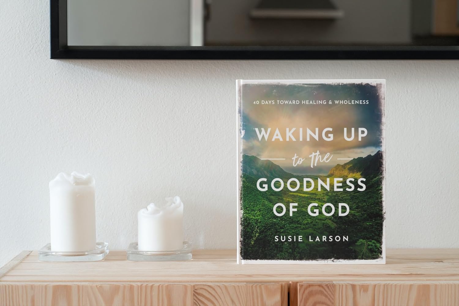 Book titled 'Waking Up to the Goodness of God' by Susie Larson on a wooden surface with candles.